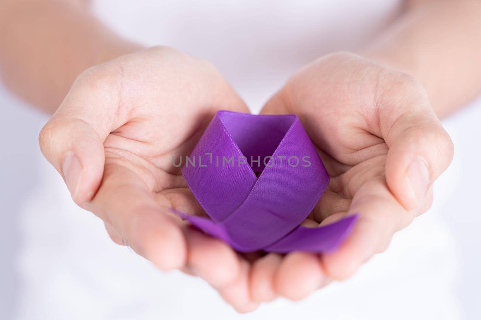 World cancer day, hands holding purple ribbon on grey background. Healthcare and medical concept. by mikesaran