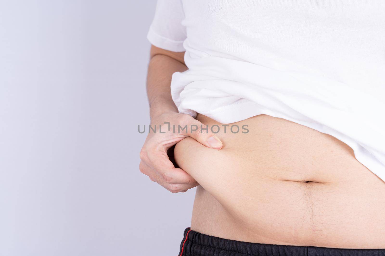 Fat man holding excessive fat belly, overweight fatty belly isolated grey background. Diet lifestyle, weight loss, stomach muscle, healthy concept.
