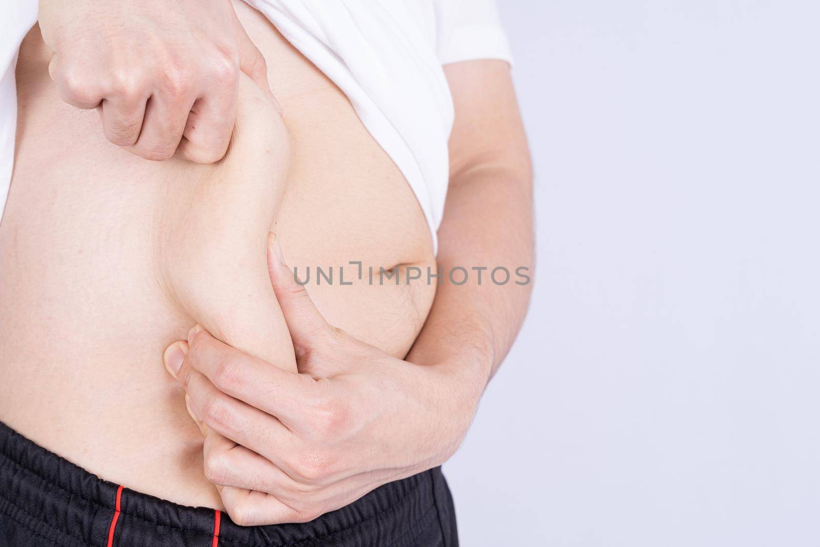 Fat man holding excessive fat belly, overweight fatty belly isolated grey background. Diet lifestyle, weight loss, stomach muscle, healthy concept.