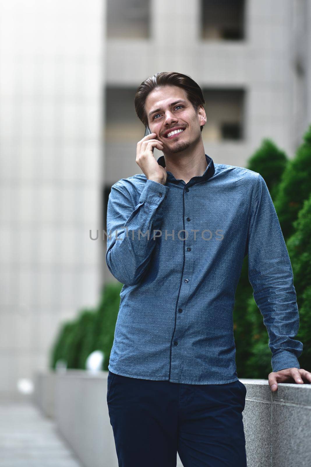 Nice positive guy in smart casual style is talking on the phone among the City landscape. by Nickstock