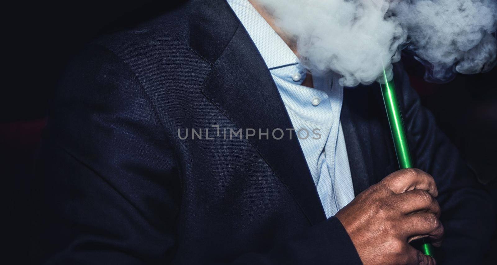 a man with no face smokes a hookah slowly exhaling smoke at the nightclub by Nickstock