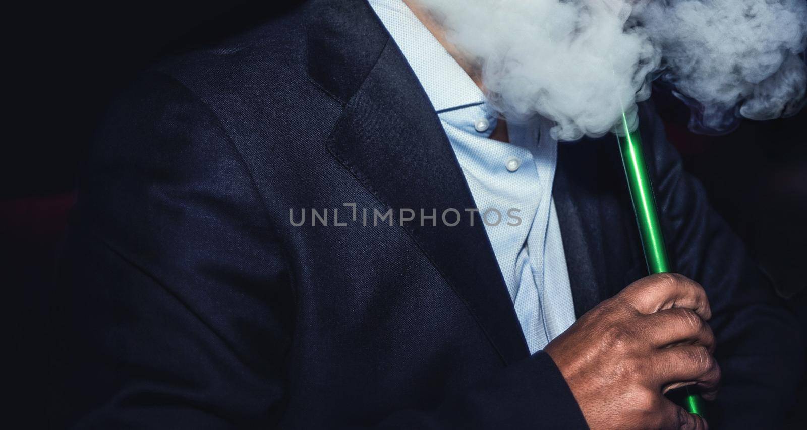 a man with no face smokes a hookah slowly exhaling smoke at the nightclub