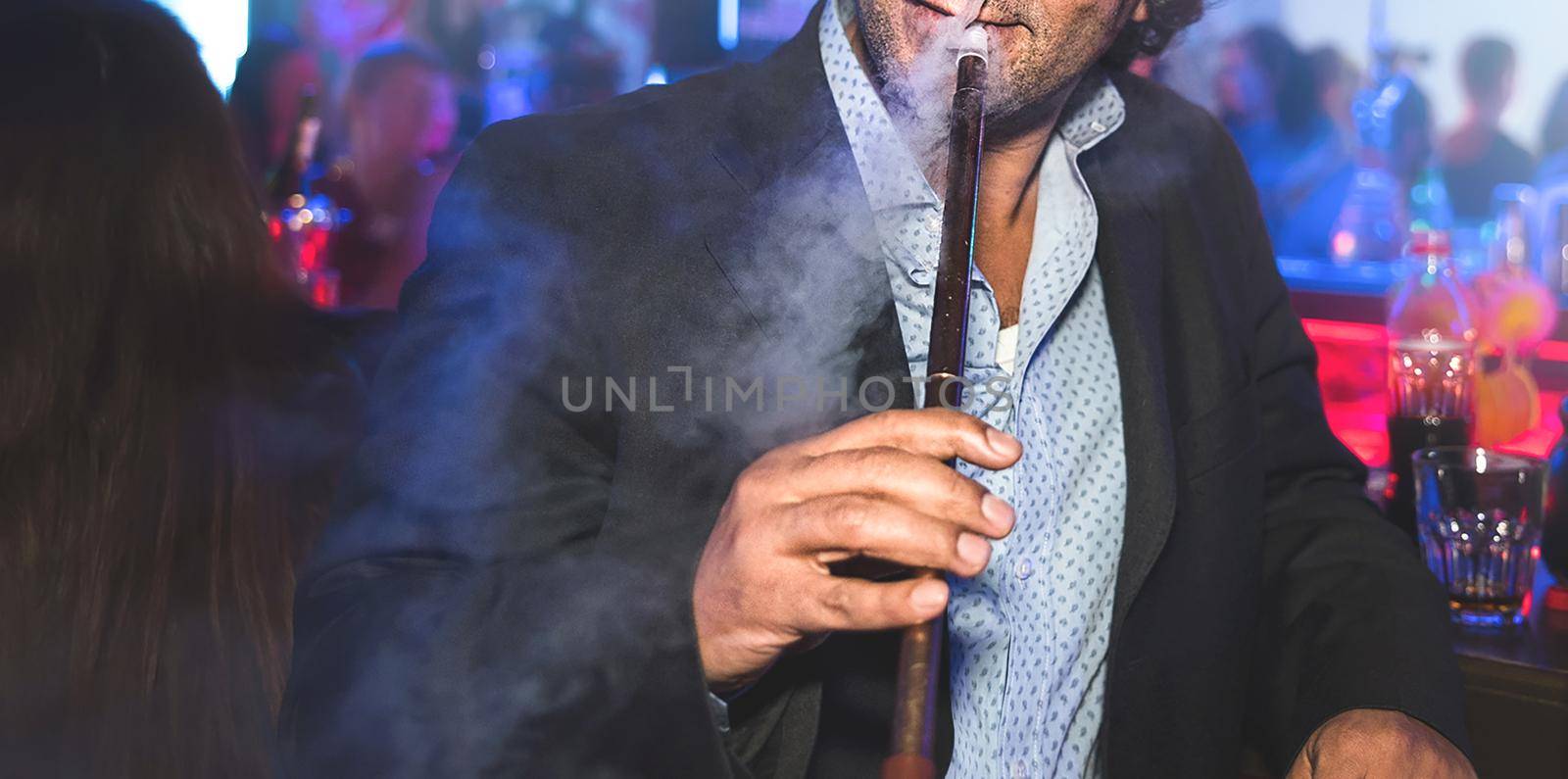 a man with no face smokes a hookah slowly exhaling smoke at the nightclub