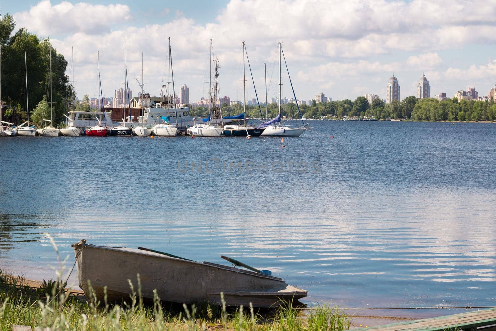Small fishing boat standing near marina with sailing yachts on river bank