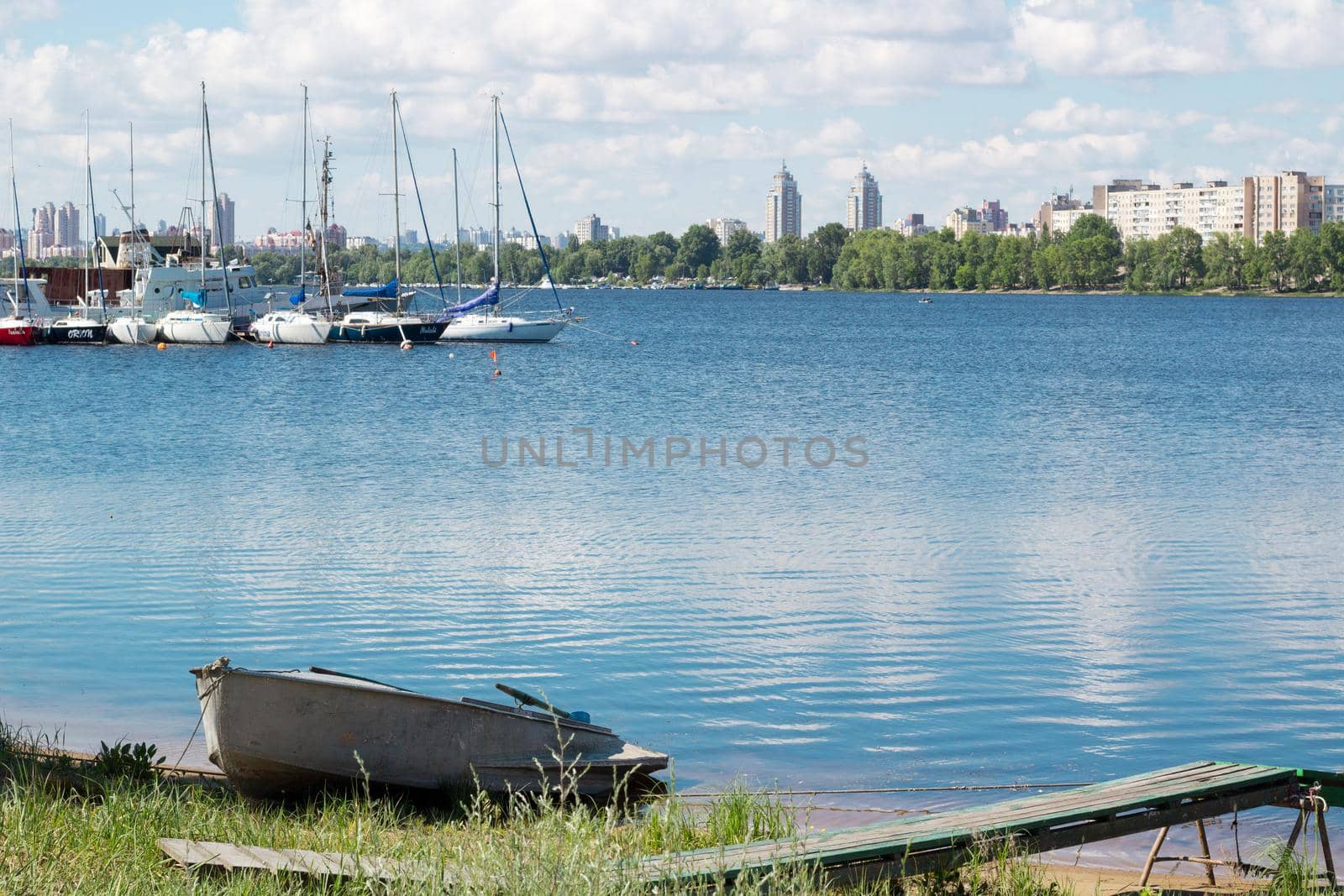 Small fishing boat standing near marina with sailing yachts and boats on river bank