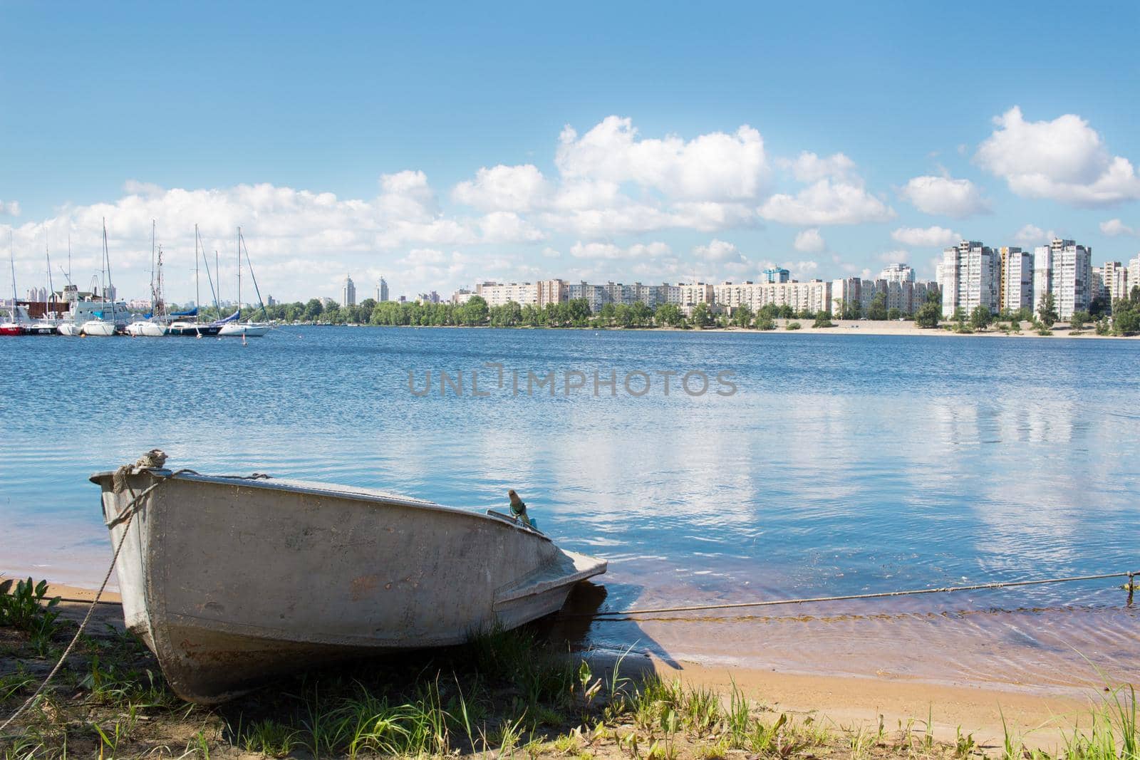 Small fishing boat near marina with sailing yachts on river bank