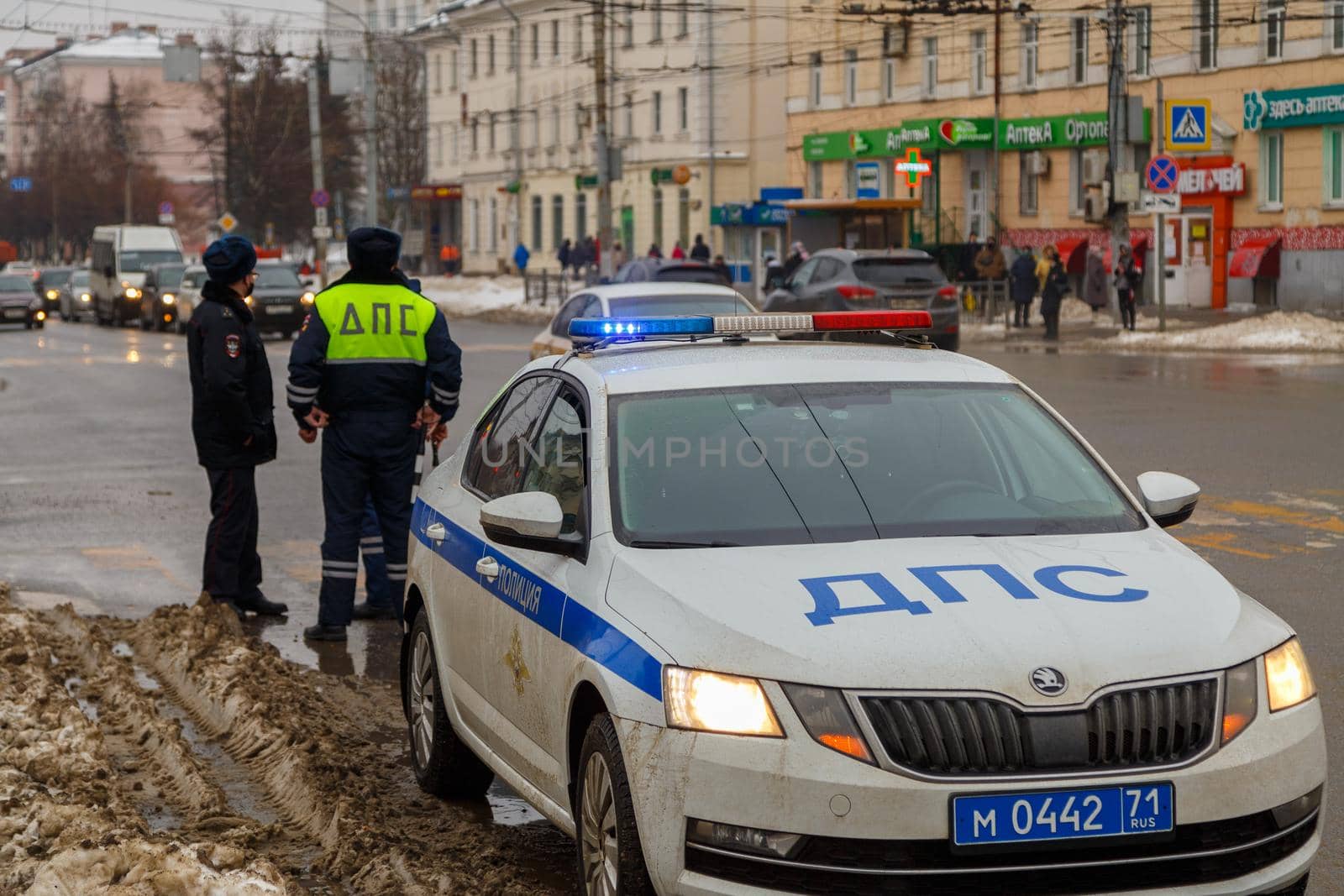 Russian road police officers standing near patrol car and dirty snow on winter city road - close-up with selective focus on roof lamp. Letters DPS mean Traffic Patrol Police