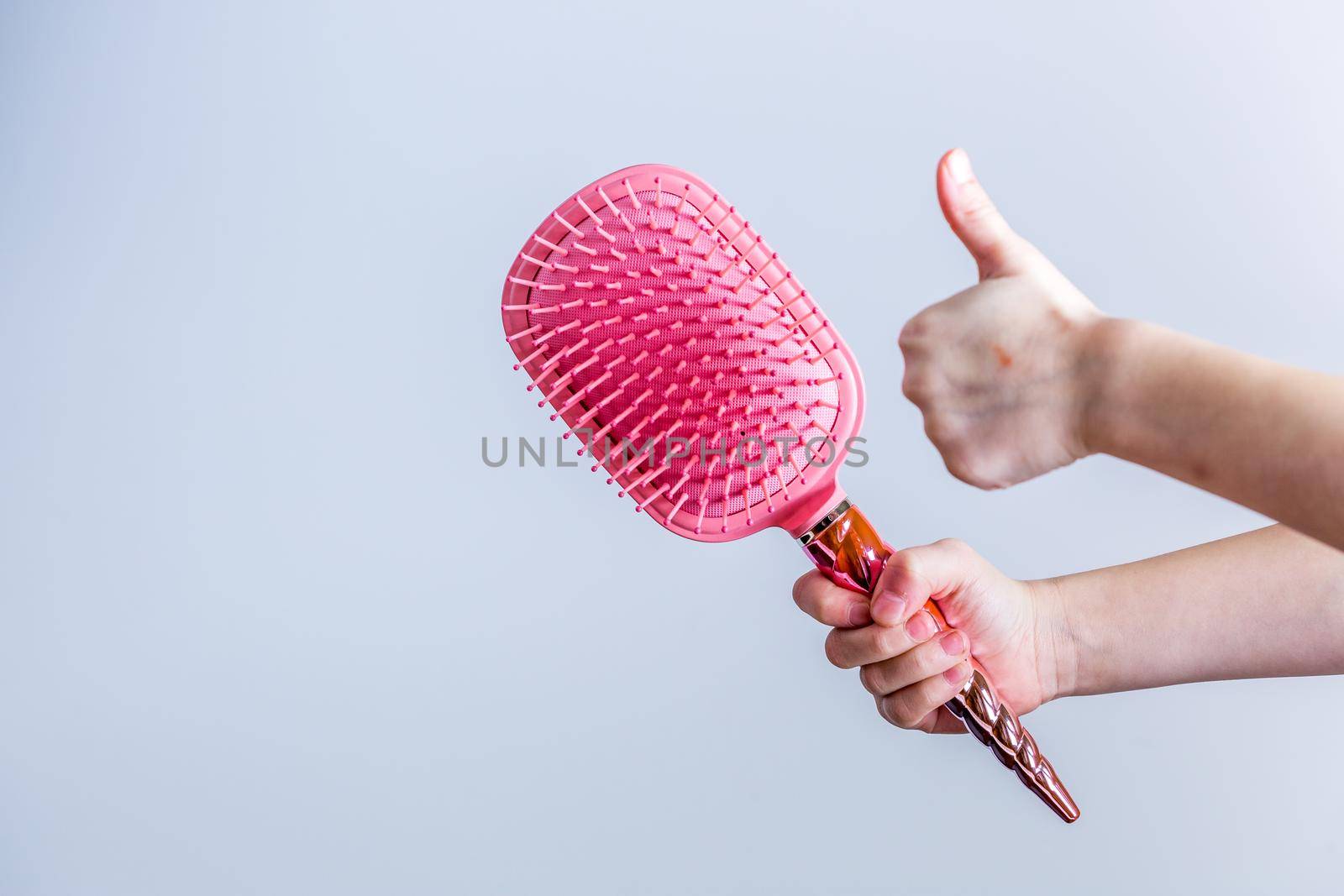 Beautiful pink comb brush in the hand of a girl with thumb up on white background. Women's Hair Care Accessories. Side view