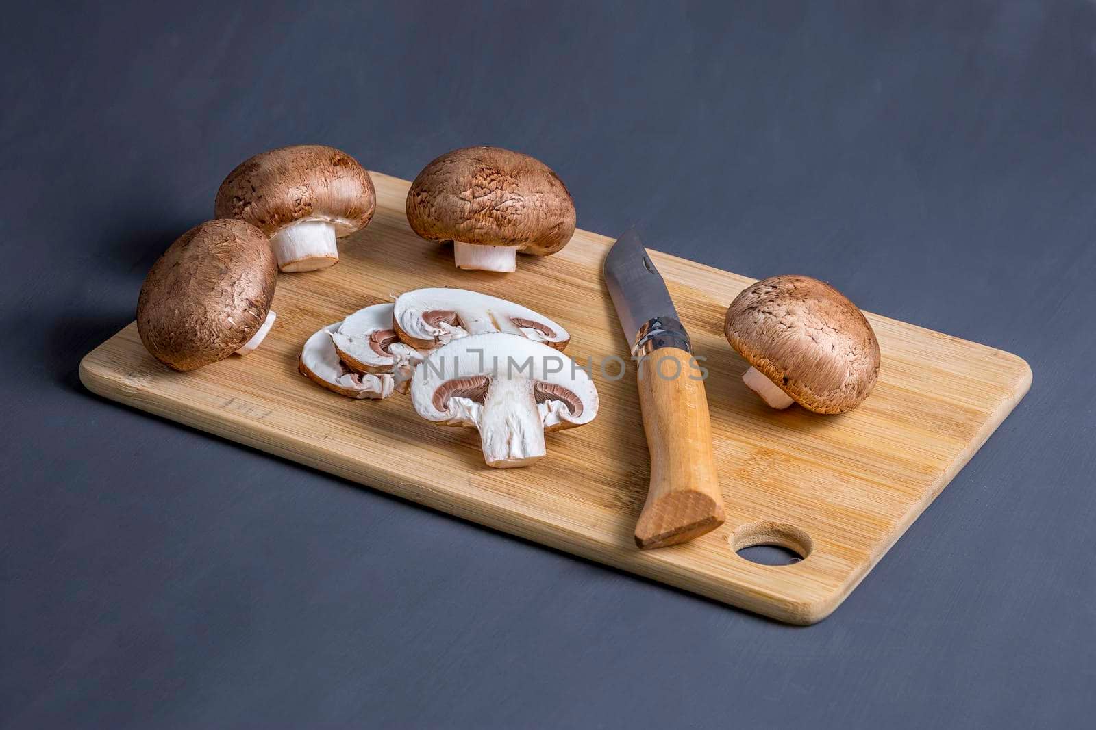 Royal champignons, Parisian champignons, chopped mushrooms on bamboo wooden chopping board, close-up. Dark wooden background. Side view.