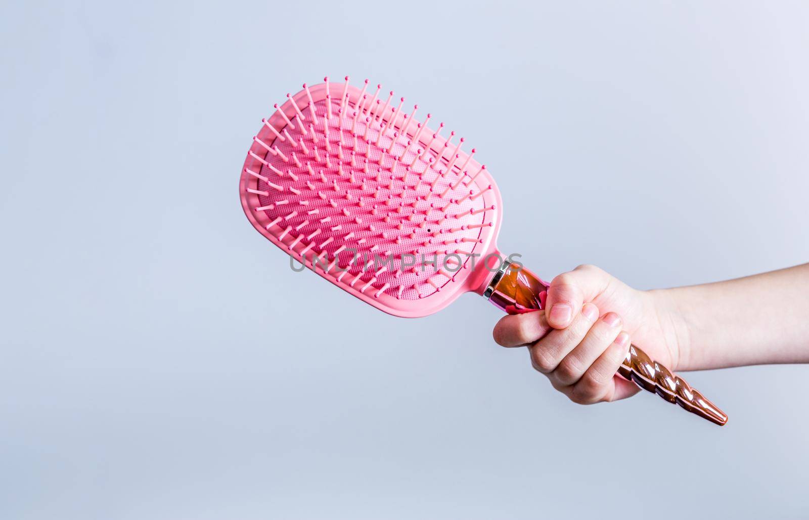 Beautiful pink comb brush in the hand of a girl on a white background. Women's Hair Care Accessories. Side view