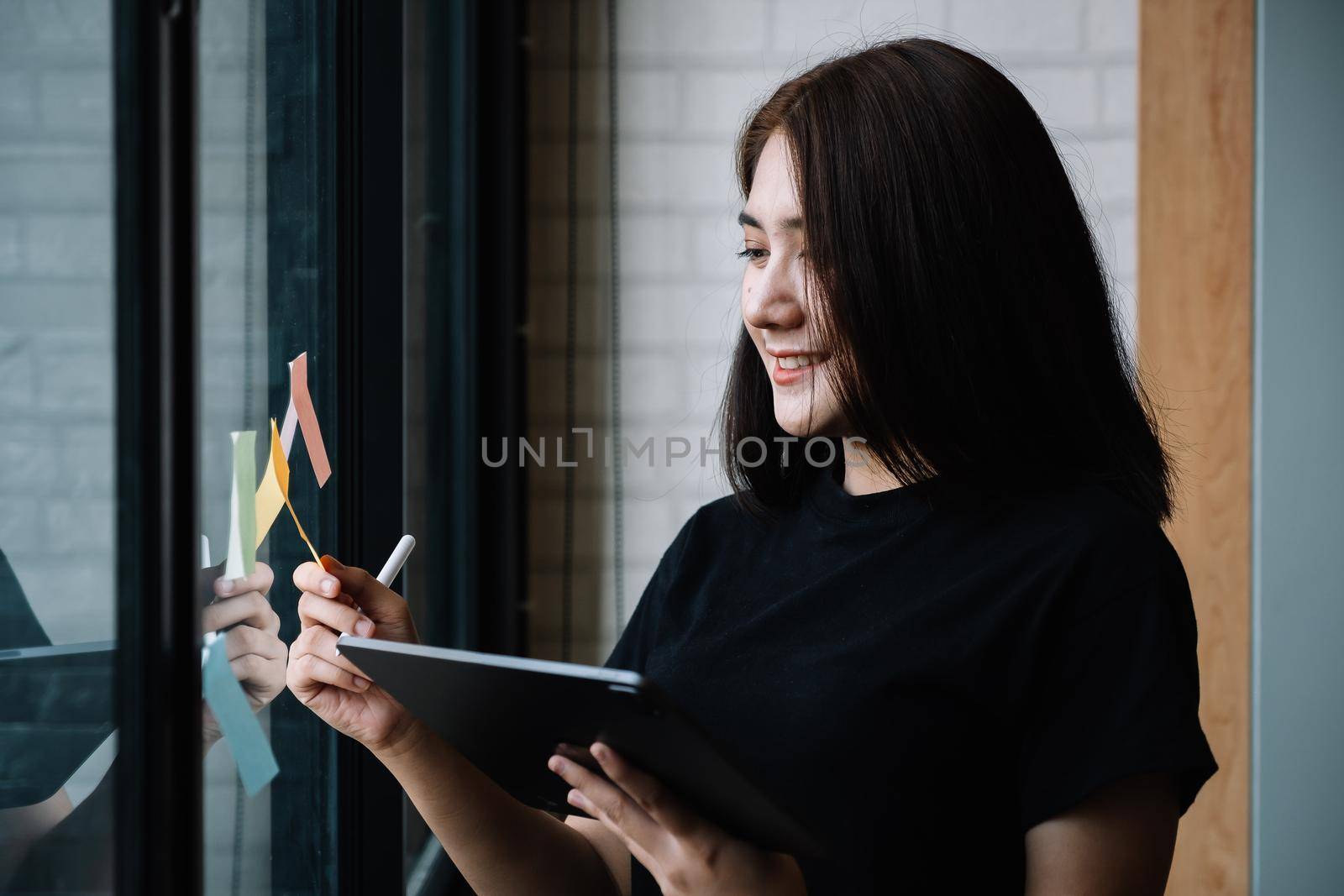 business woman using tablet during post it notes idea discussing and planning in glass wall at meeting room, business concept. by nateemee
