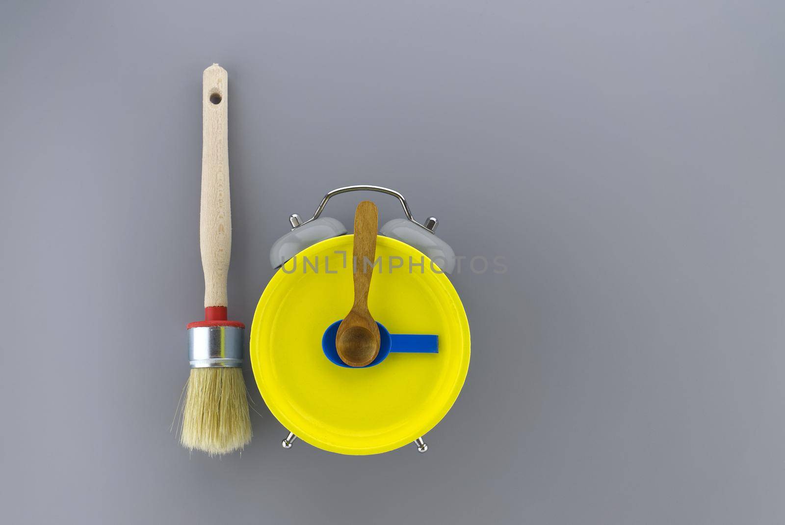 Creative DIY, decorating or renovations background with two clean bristle brushes and a colorful yellow alarm clock with tools for hands forming a border on grey with copy space