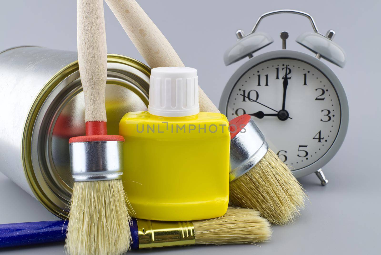 New color, decorating or renovations concept with a still life of an alarm clock with assorted clean paint brushes and unlabeled tin of paint over a grey background