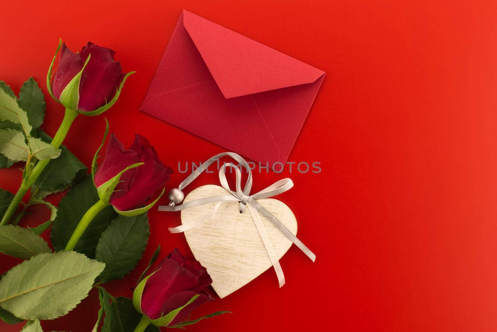 Red roses, envelope and wooden heart medallion on red background with free copy space. Wishes, greetings and love message