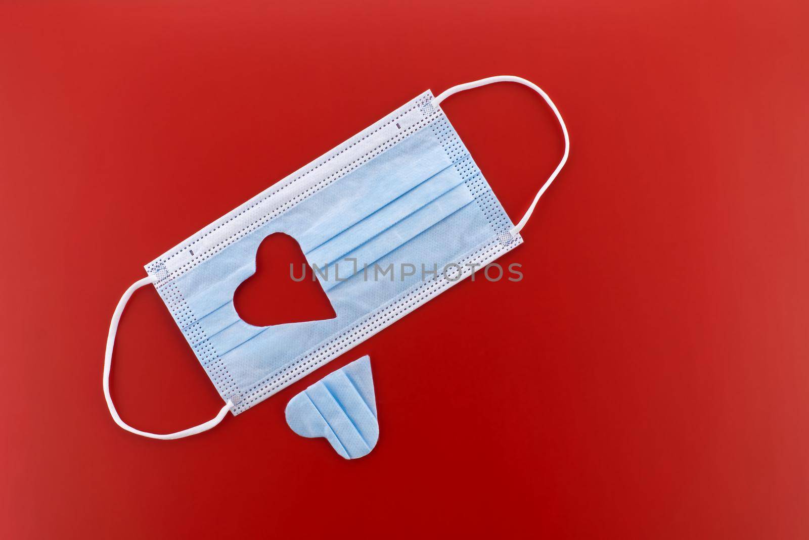 Face mask with a cut-out heart shape over red background with free copy space