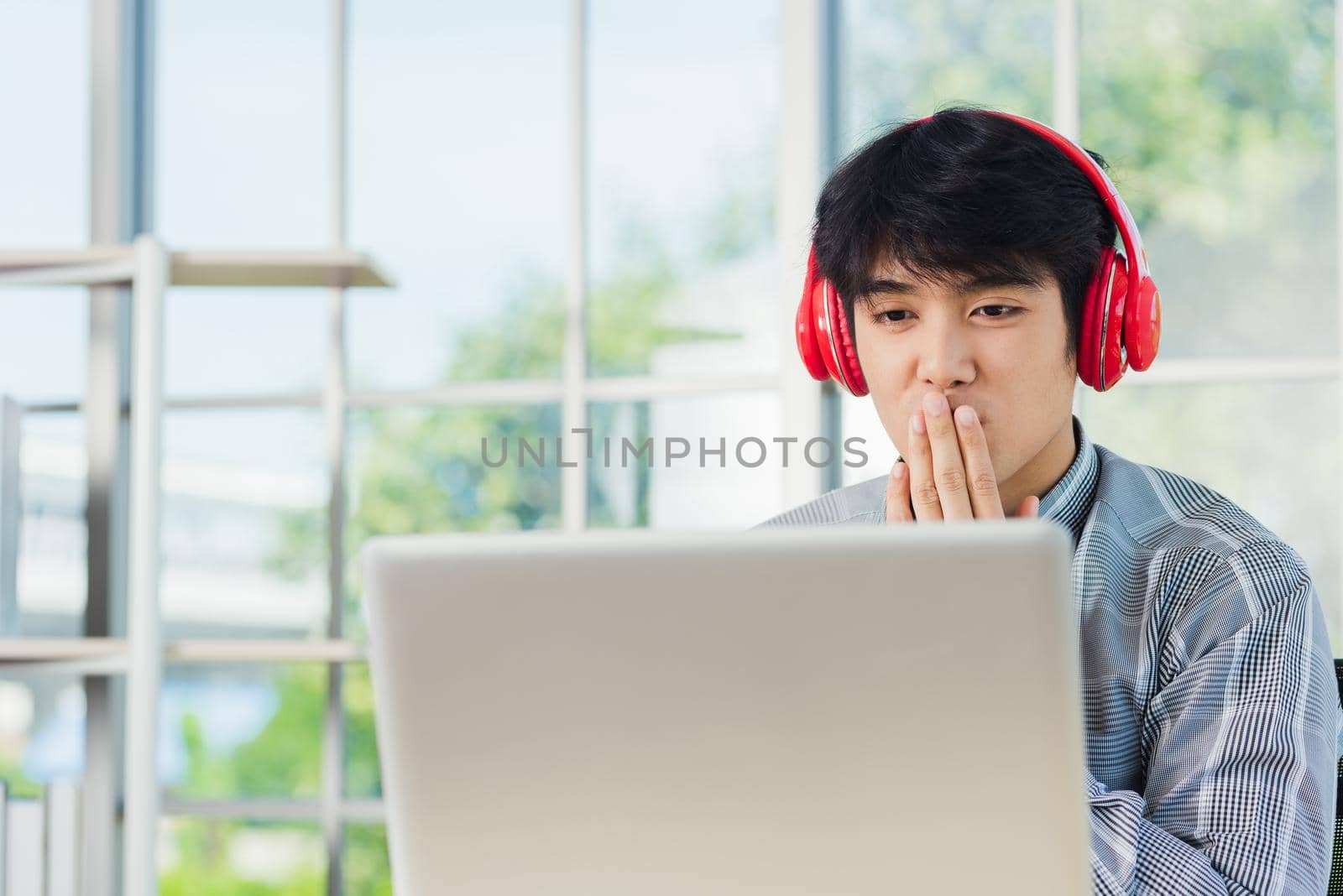Asian young businessman happiness with red headphones he sitting on desk workplace home office looking to laptop computer monitor, confident handsome man lifestyle smile relax he listens to music