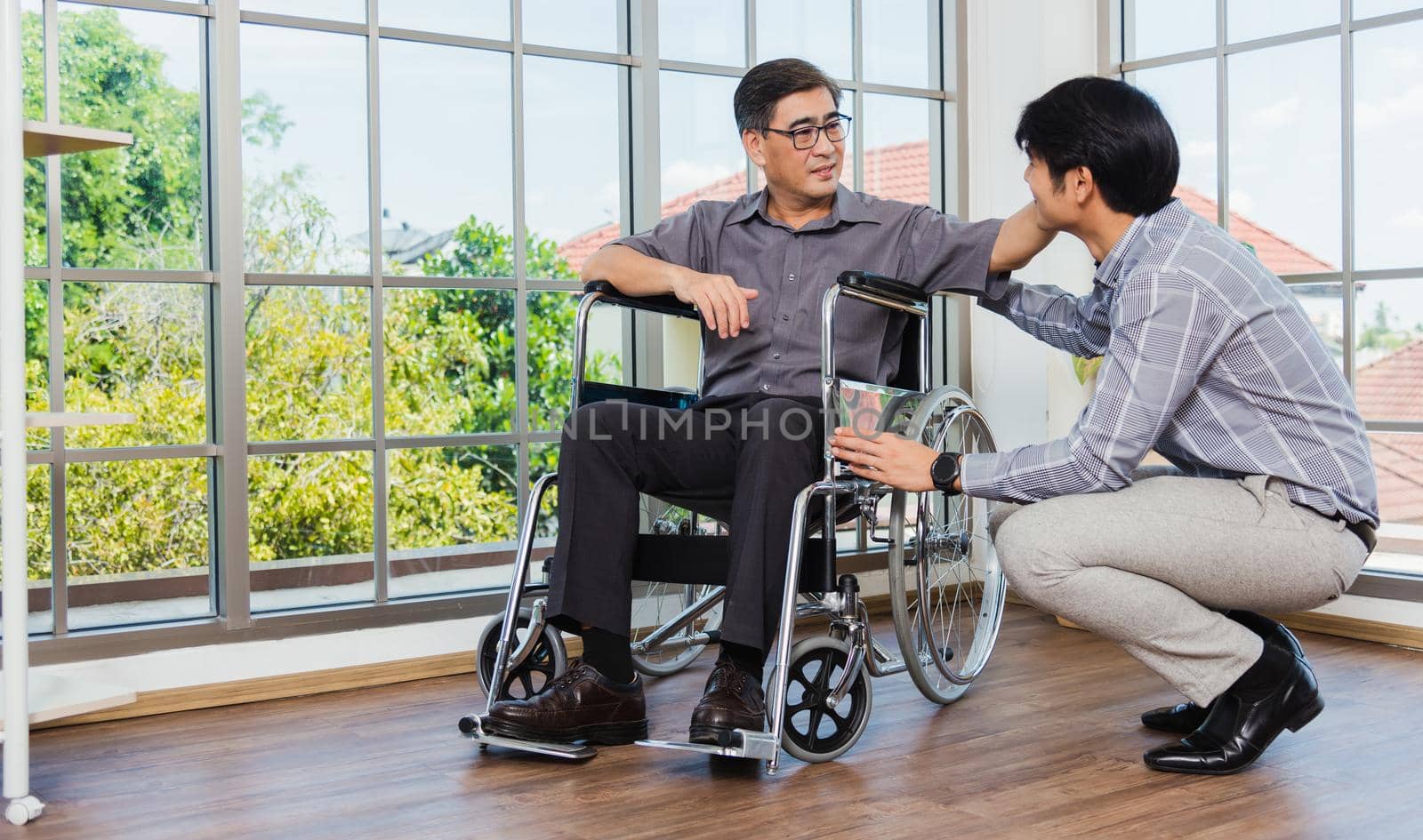 Asian senior disabled businessman in wheelchair discuss interacting together with the team in the office. The old man in a wheelchair and his young son talking to and comforting bound father