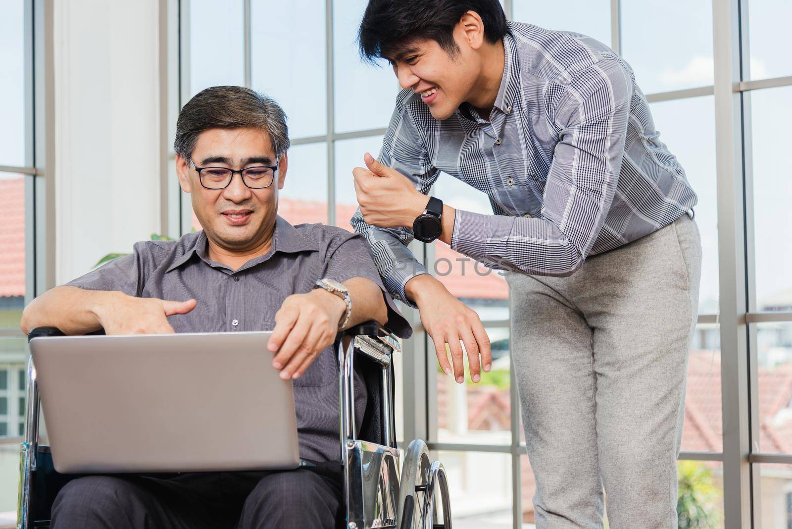 father man sitting wheelchair and his son talking video calls conference on laptop by Sorapop