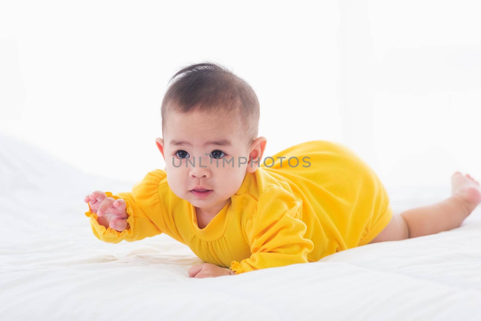 Portrait of beautiful young Asian newborn little baby prone on the bed at home, Happy baby smile wears a yellow shirt relaxing in the room, Family morning at home