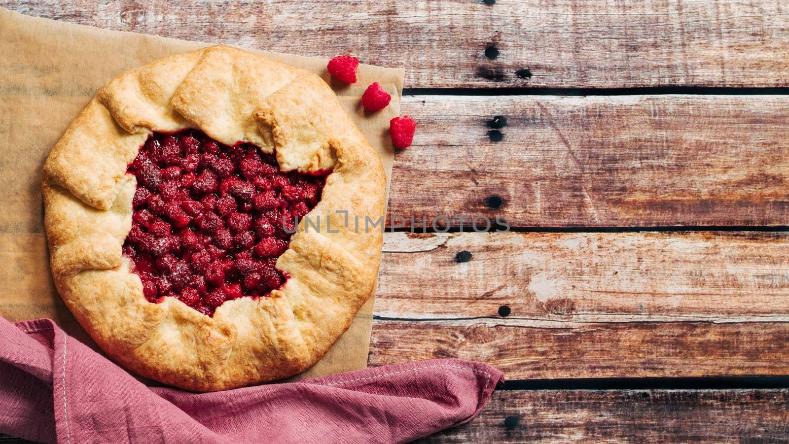 Perfect raspberry galette. Delicious rustic homemade tart with frozen or fresh raspberries on old wooden background. Beautiful round shape galette with raspberries,copy space. Top view or flat lay