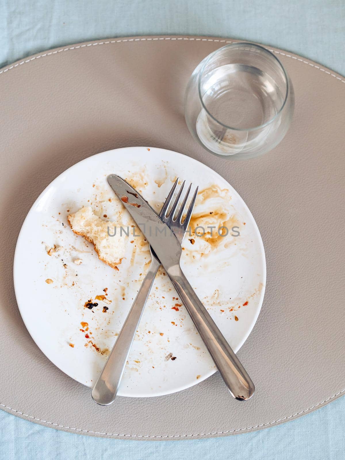 dirty plate after eating on the dining table. Top view of dirty white plate with crosswise cutlery over blue linen tablecloth. Vertical