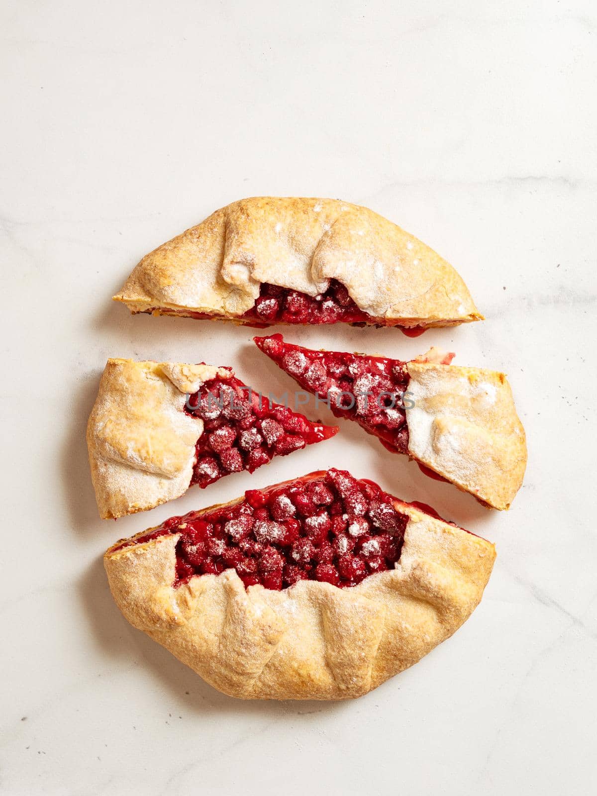 Perfect cut raspberry galette. Delicious rustic homemade tart with frozen or fresh raspberries on white marble background. Beautiful round shape galette with raspberries,copy space. Top view, flat lay