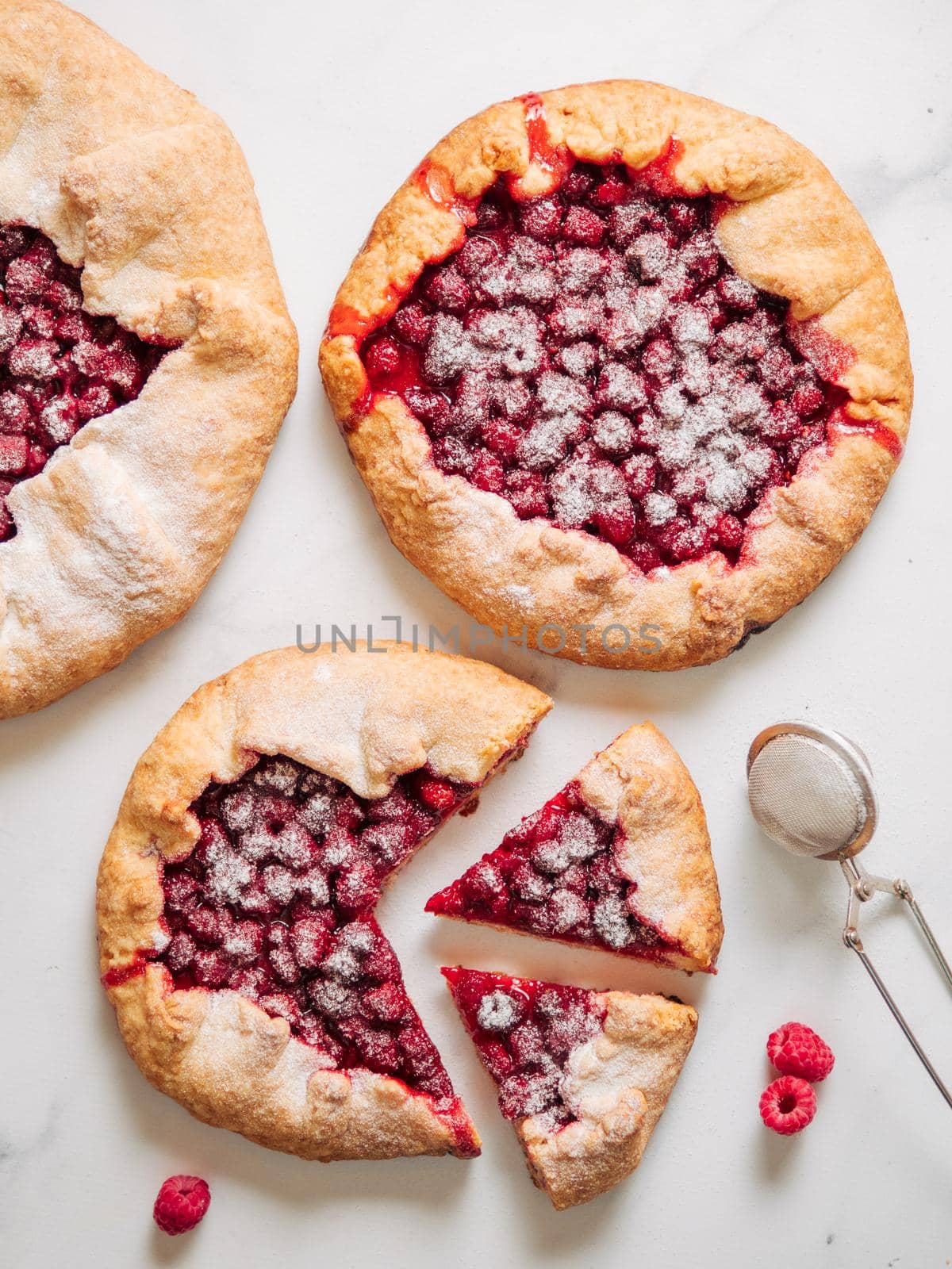 Three perfect raspberry galettes. Delicious rustic homemade tart with frozen or fresh raspberries, marble background. Beautiful galettes with raspberries, copy space. Vertical. Top view or flat lay