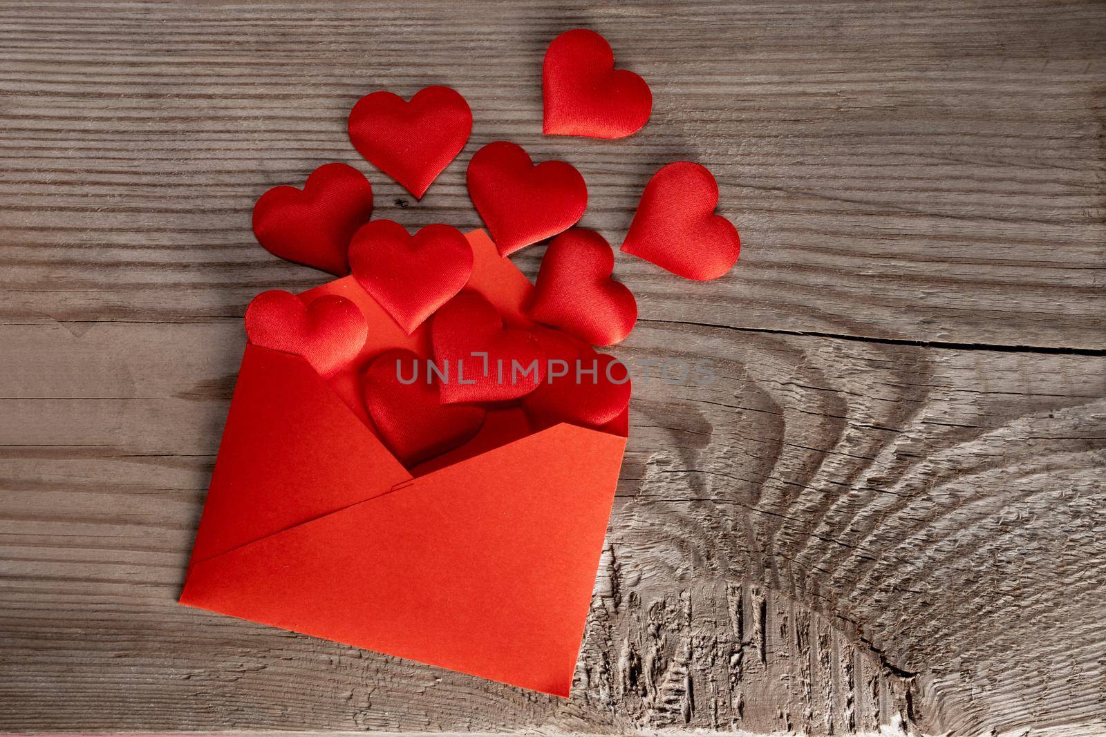 Valentine day love letter, envelope with red hearts heap spread on wooden background