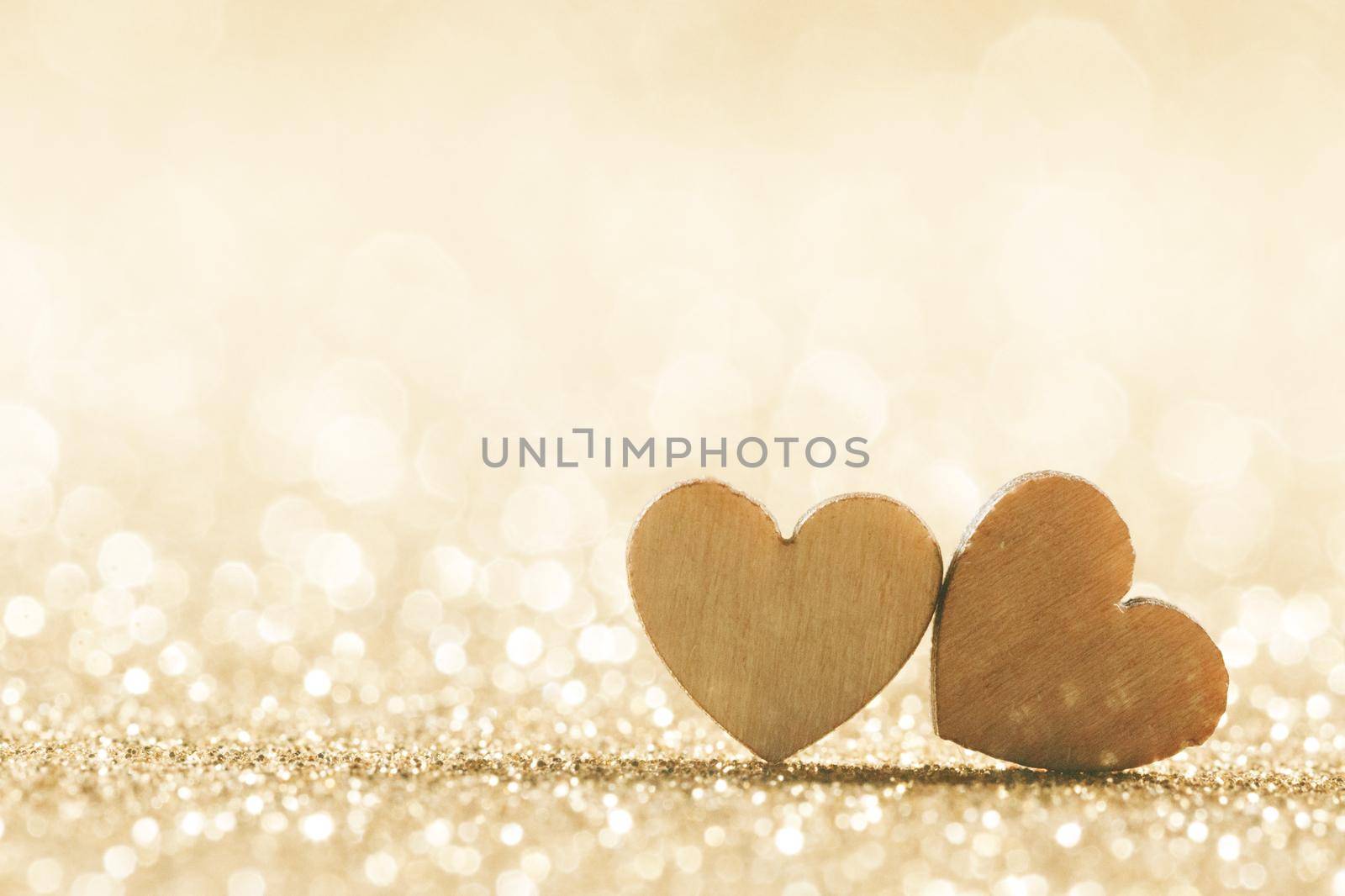 Two small handmade wooden hearts on bright golden lights bokeh background Valentines day card