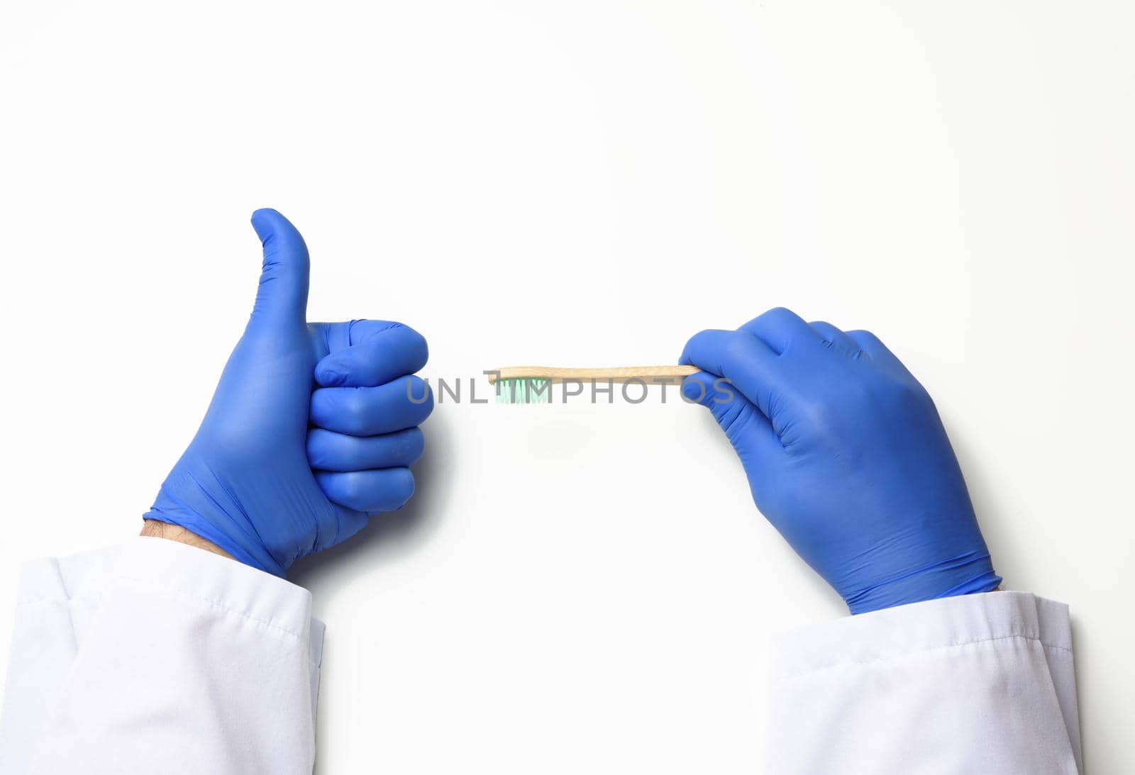 doctor therapist is dressed in a white robe uniform and blue sterile gloves holding a toothbrush, daily brushing concept, white background