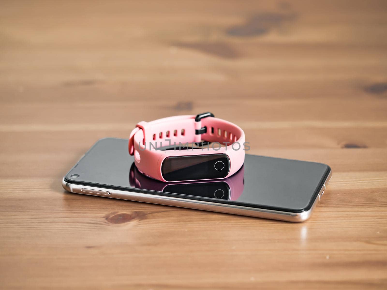 Fitness tracker on smartphone wooden tabletop. Pink female pedometer or wearable device on smartphone with infinity display, copy space