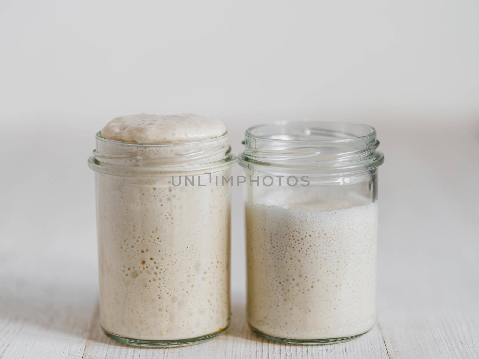 Two glass jars with wheat sourdough starters in different hydration levels. Starter 100 percent hydration (left) and starter with higher hydration (right). Copy space