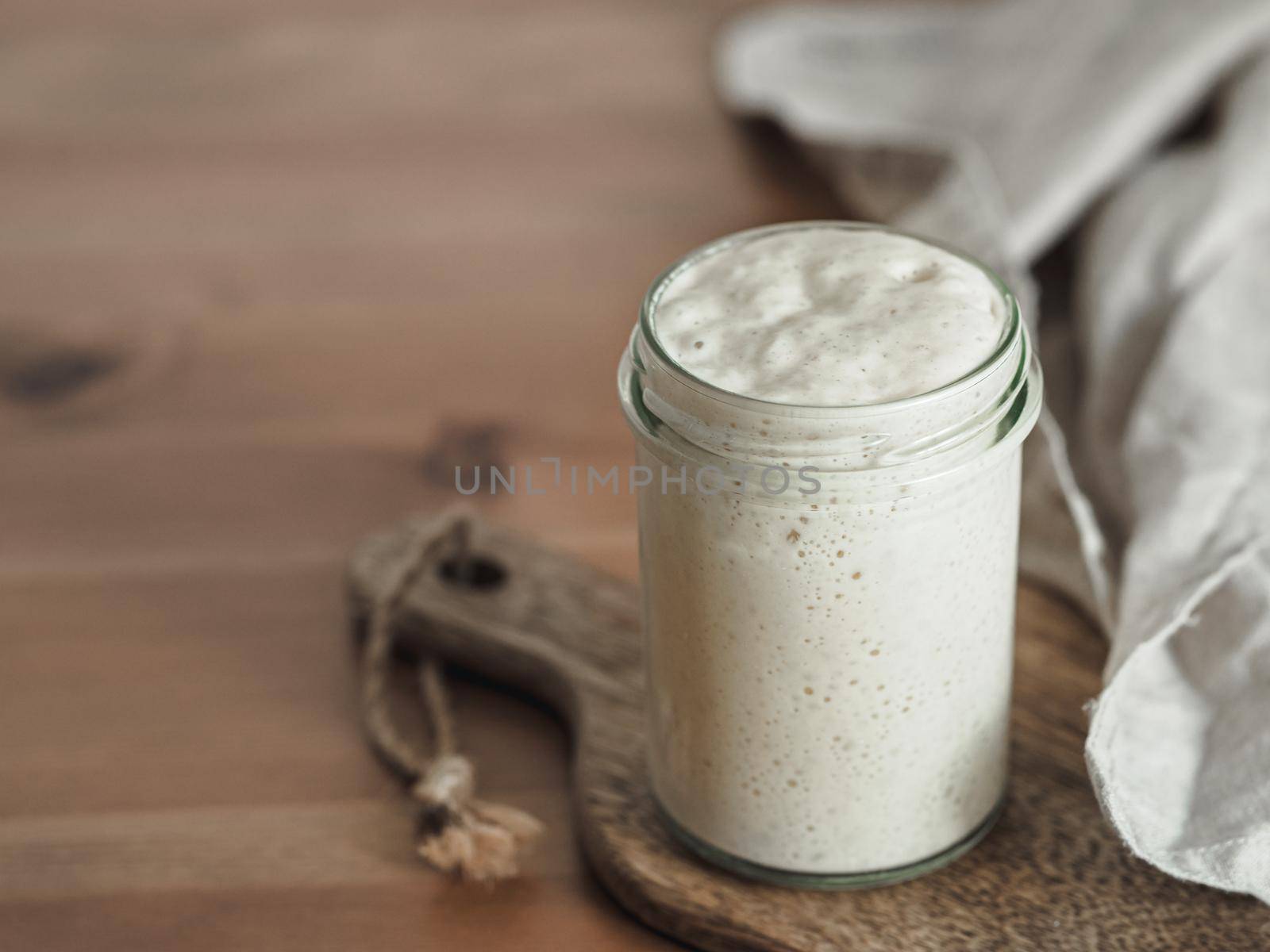 Wheat sourdough starter. Glass jar with sourdough starter on wooden cutting board over wooden tabletop. Copy space for text or design.
