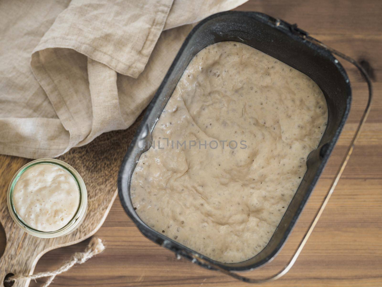 Wheat sourdough starter in glass jar and sourdough in bread pan of bread maker machine. Homemade breadmaking concept