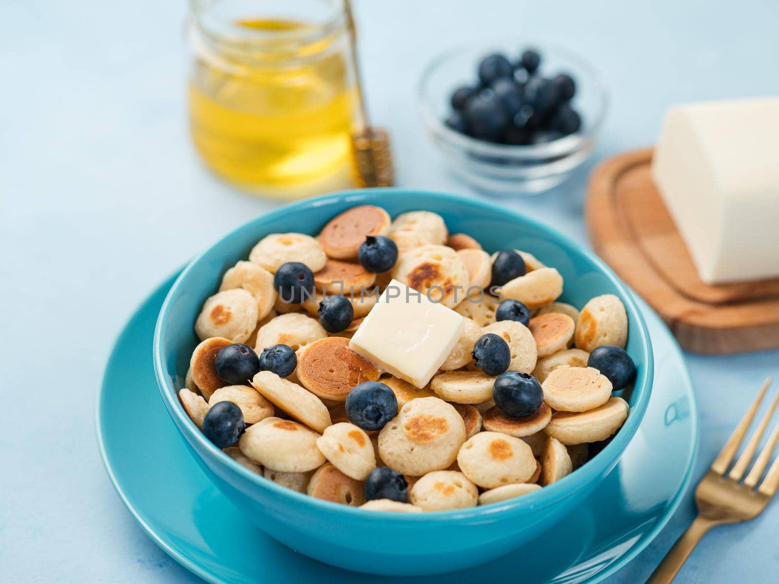 Trendy food - pancake cereal. Heap of mini cereal pancakes in boul on blue background. Copy space for text or design