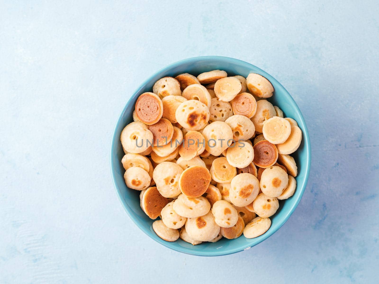 Trendy food - pancakes cereal. Heap of mini cereal pancakes in boul on blue background. Copy space left for text. Top view or flat lay.