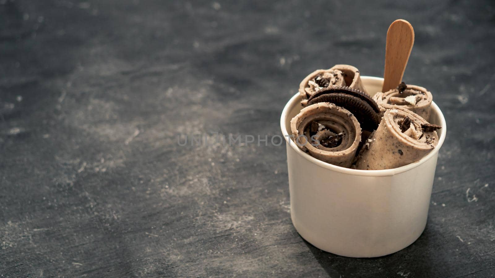 Rolled ice cream with in cone cup on dark rustic background. Iced rolls with biscuits chocolate sandwich cookies. Thai style rolled ice cream with copy space for text or design. Banner.