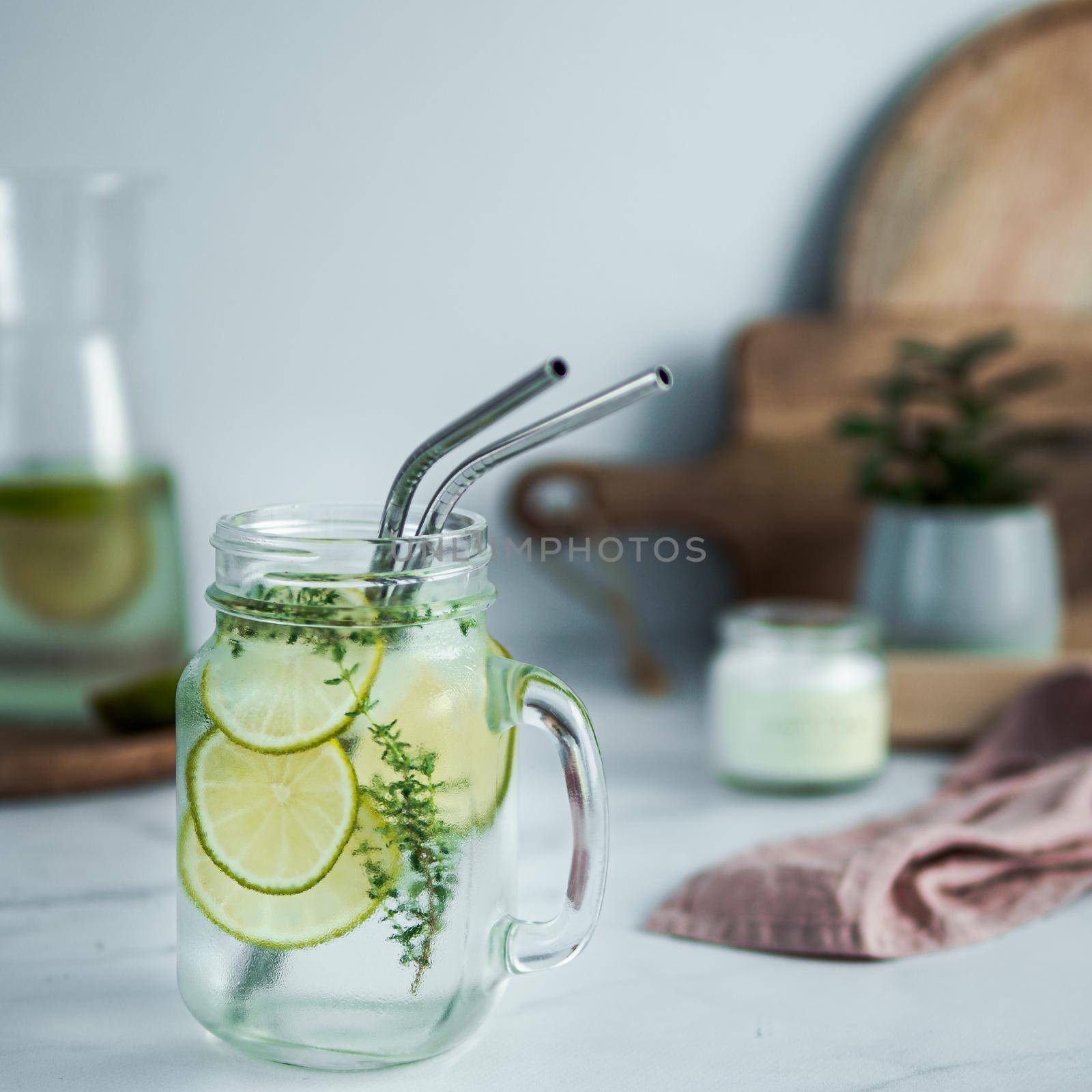 Cold drink in mason jar with metal straws on kitchen table. Lemonade or detox water with lime and thyme in glass jar wit metal straw indoor. Recyclable straws, zero waste concept