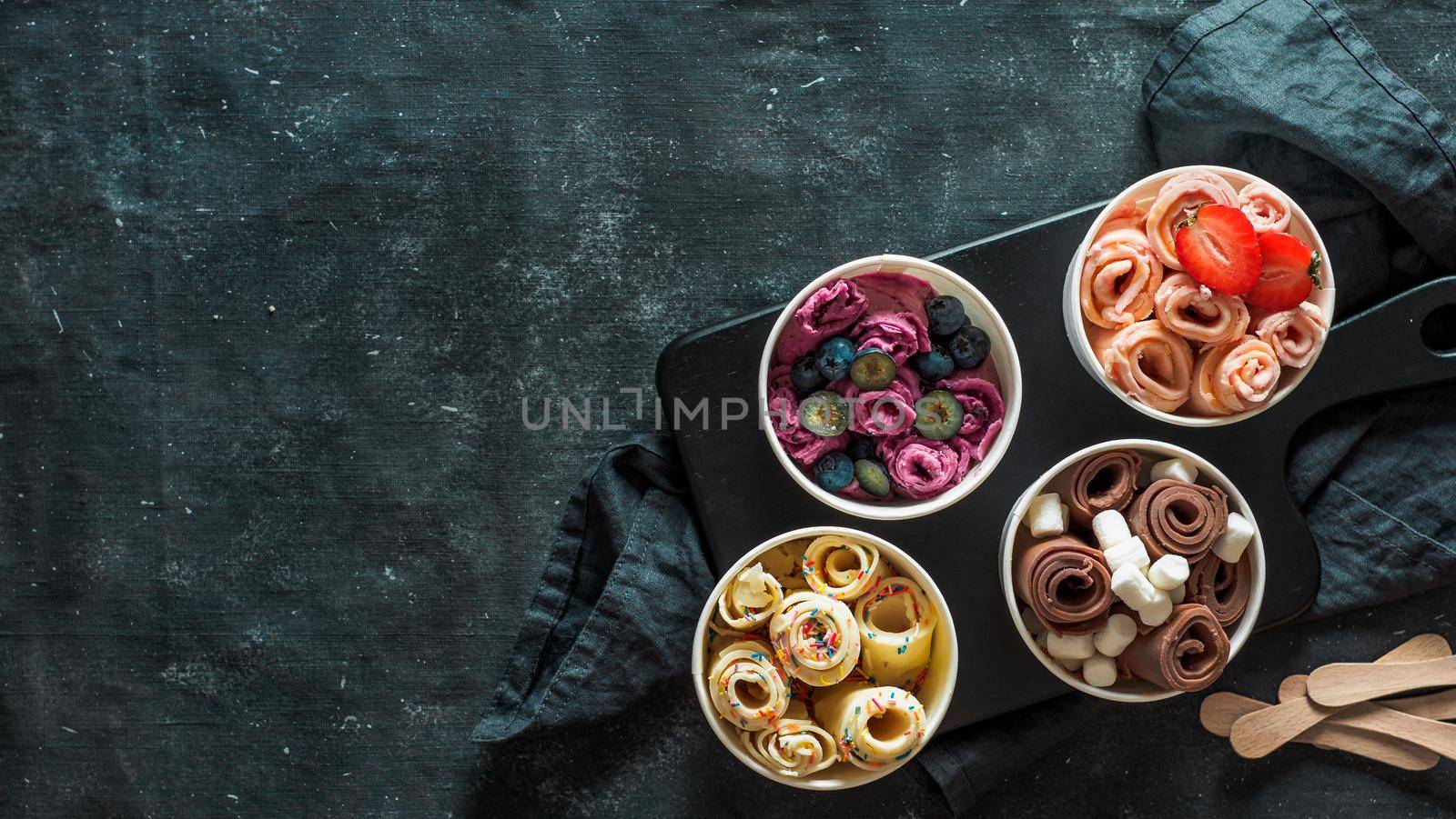 Rolled ice cream in cone cups on dark background. Different iced rolls top view or flat lay. Thai style rolled ice cream with copy space in center for text or design. Banner
