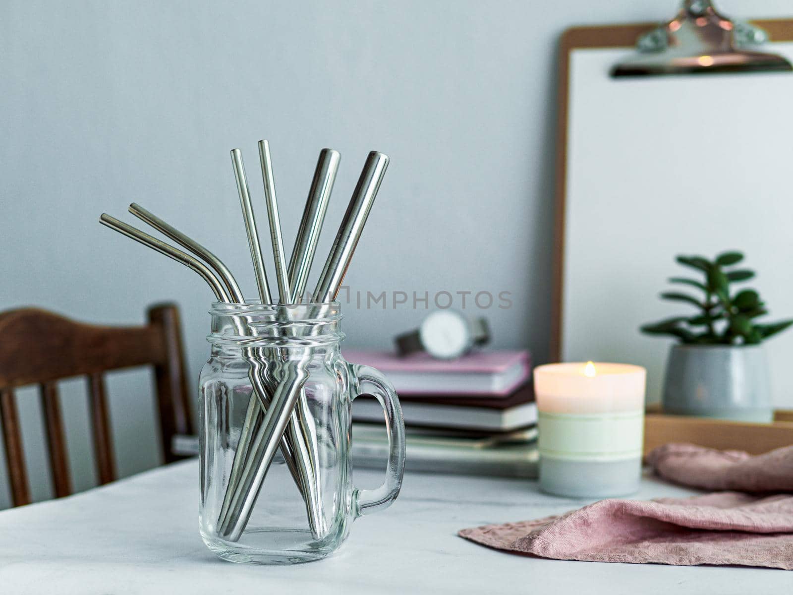 Metal drinking straws in glass bottle on white marble table indoor. Metal straws on table in living room interior. Recyclable straws, zero waste concept.