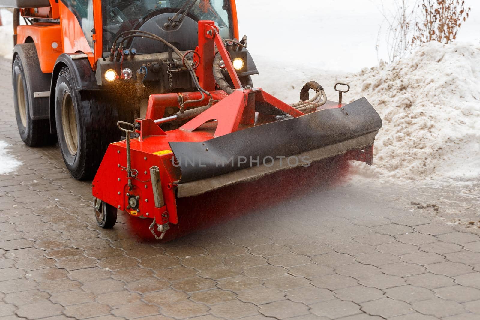 Snow cleaning process at winter city. Snow removal tractor clearing snow from pavement with special round spinning brush.