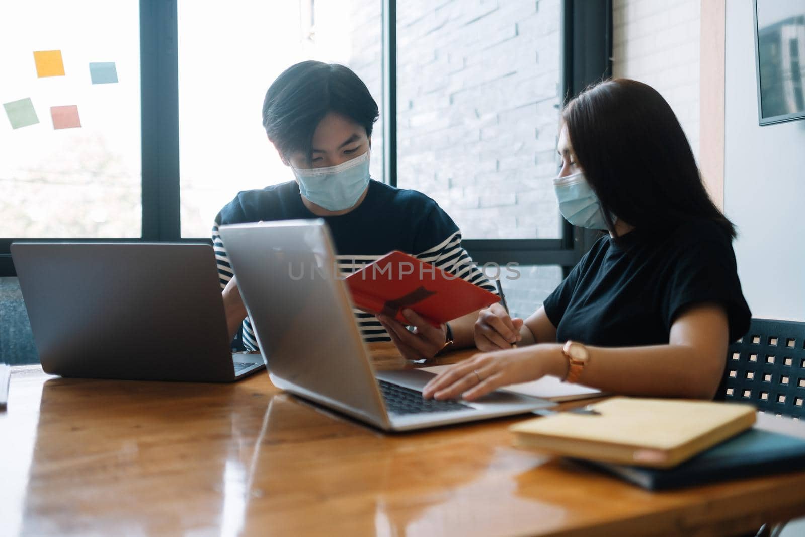 Asian woman and man workers meeting together with laptop for financial and wear protective masks prevent corona virus or covid19 at co working space .Health and teamwork concept. by nateemee