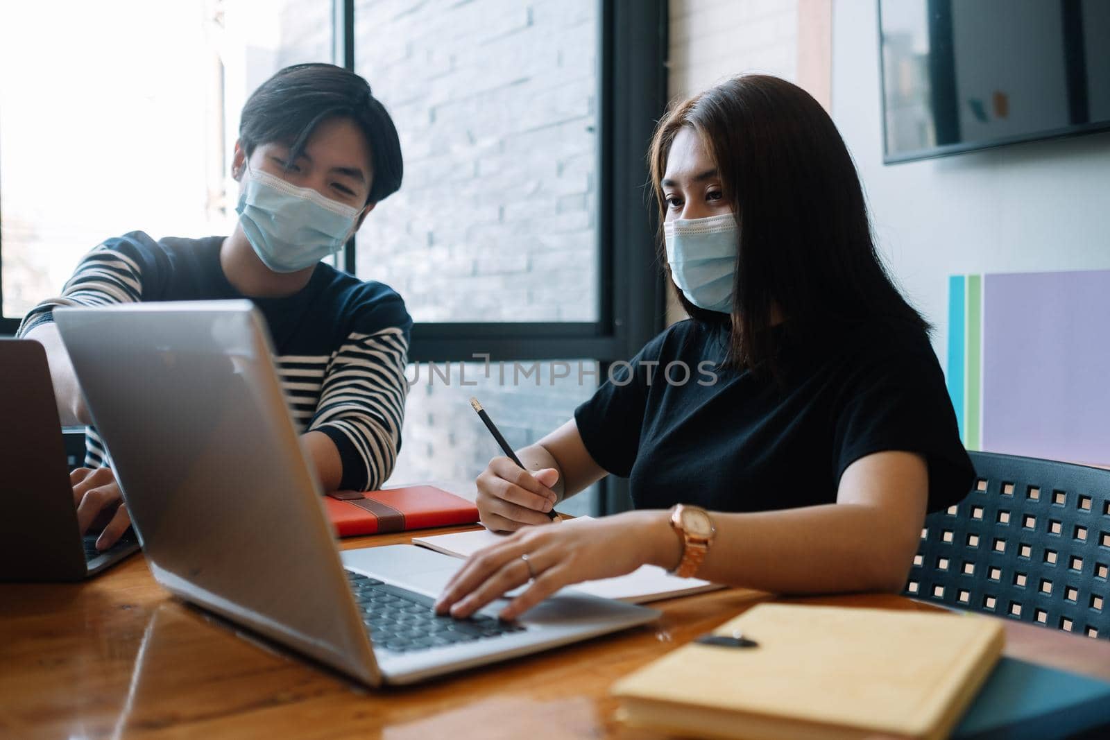 Asian woman and man workers meeting together with laptop for financial and wear protective masks prevent corona virus or covid19 at co working space .Health and teamwork concept. by nateemee