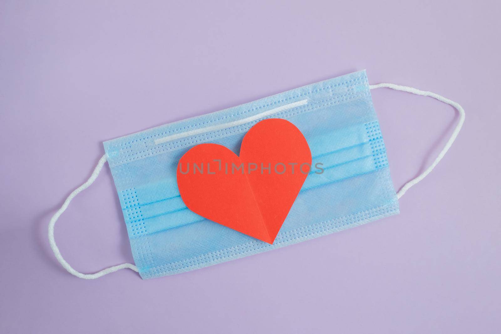 COVID-19. Face mask with cut paper heart on a purple background. Medical masks to protect against viruses and pollution. Concept of celebrating valentine's day in a new reality.