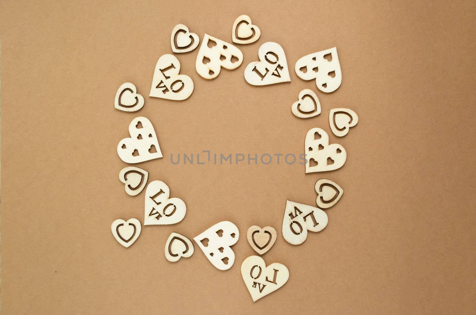 Wooden hearts on a pastel craft paper background in the form of a round frame. Abstract background with wood cut shapes. Sainte Valentine. Copy space.