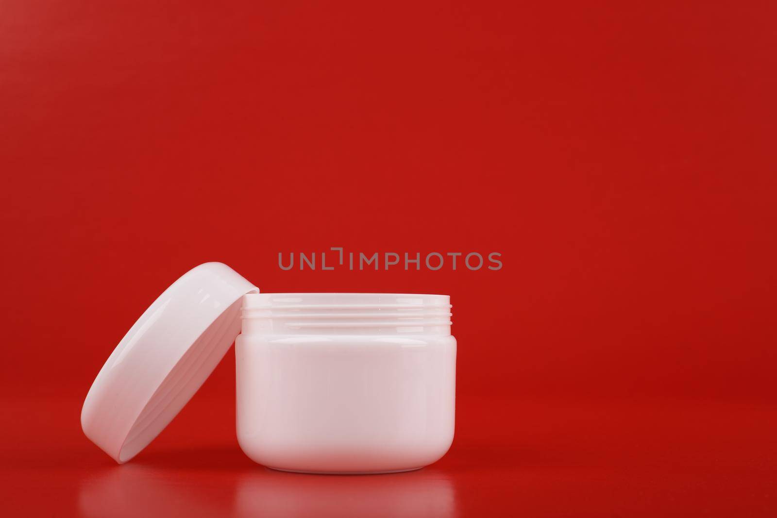 Close up of white opened jar with cream or mask against red background with copy space. Concept of beauty and luxury self treatment