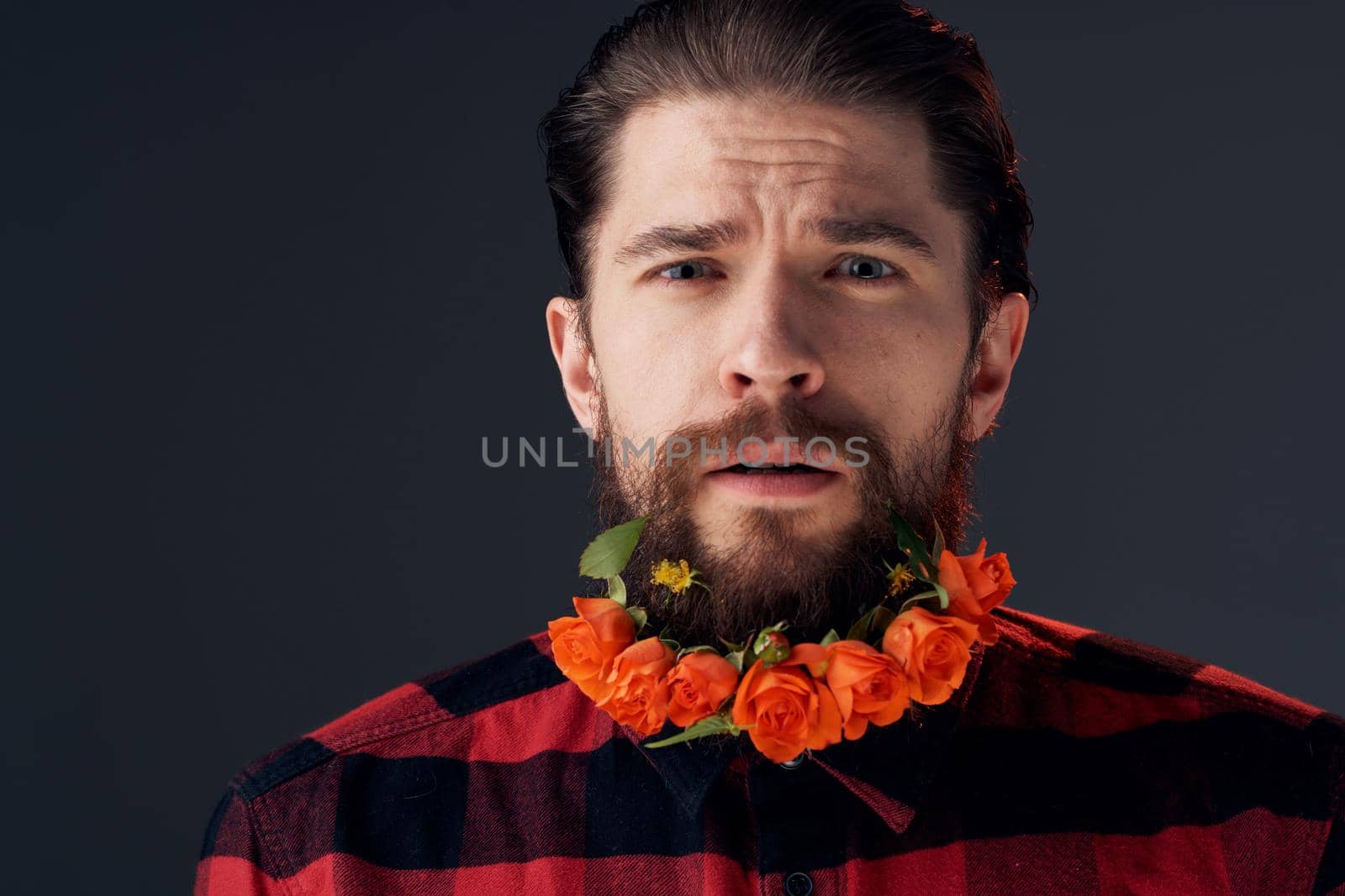 an elegant man in a plaid shirt flowers in a beard close-up dark background. High quality photo