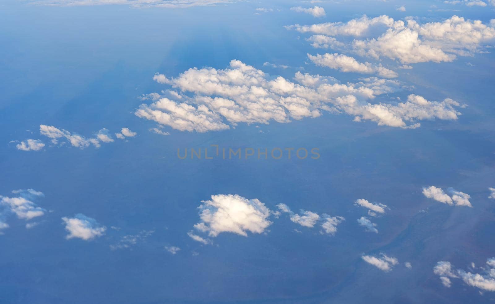 Fluffy sky clouds lit by afternoon sun, as seen from airplane flying over.