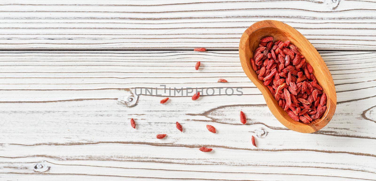 Dried goji aka. wolfberry seeds in wooden bowl and spilled on white boards desk near, view from above