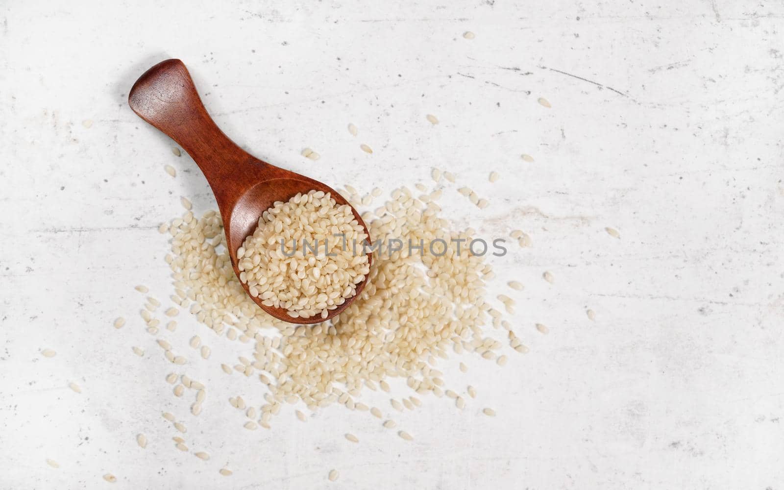 White sesame - Sesamum indicum - seeds in small wooden spoon on white stone like board, view from above.